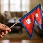 A hand holding a small national flag of Nepal after the August 2026 floods